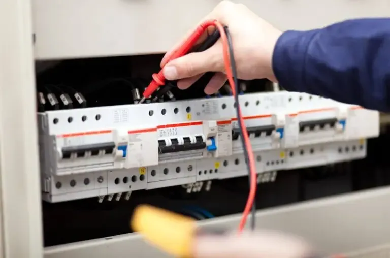 Test meter probes held against circuit breakers in a consumer unit during electrical testing